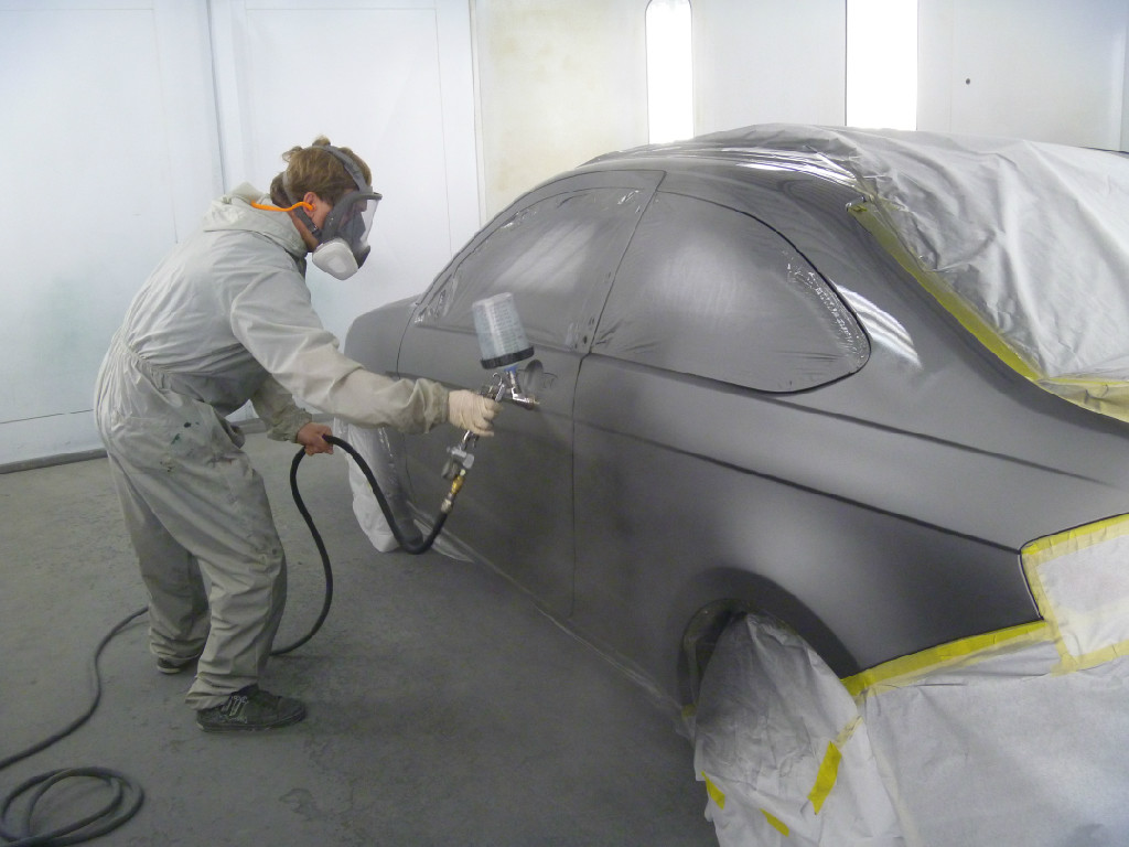 A man spraying paint on the back of a car.